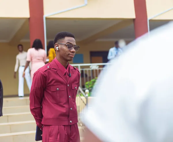 Tega in a red outfit, standing outside a building